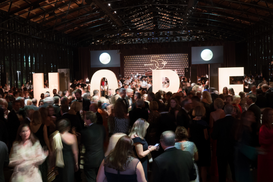 Attendees mingle at a black tie event with letters spelling HOPE illuminated in the background