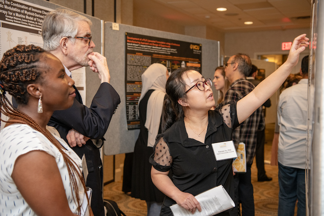 Student points to information on scientific poster in conversation with man and woman.